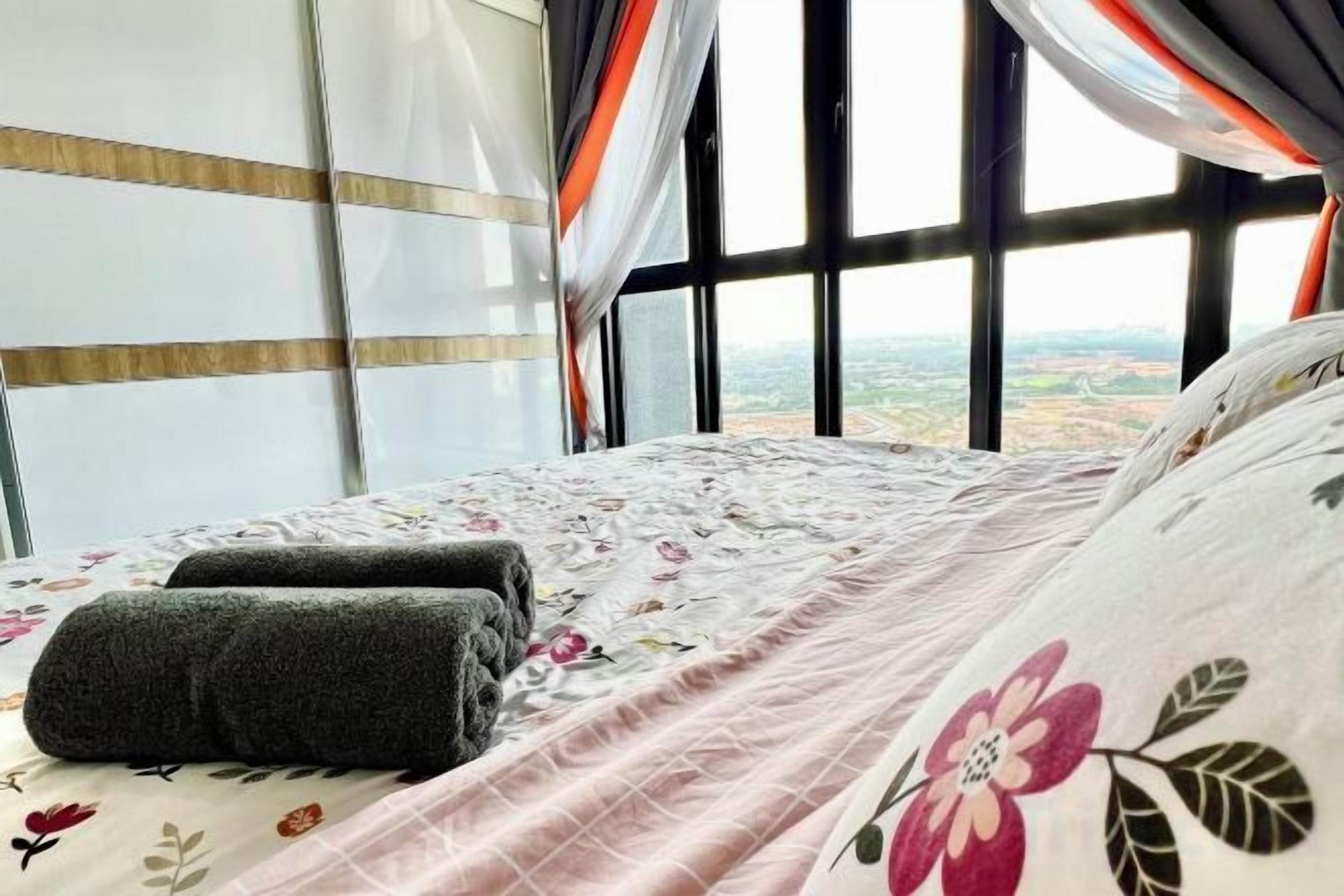 A bed with a floral bedspread and pillows, a window with curtains, and a view of the landscape.