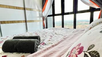 A bed with a floral bedspread and pillows, a window with curtains, and a view of the landscape.
