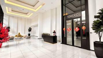 A hotel lobby with a reception desk, a large potted plant, and a modern ceiling design.