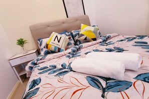Een net opgemaakt bed met een bloemenbedekking, een nachtkastje met een lamp en een kleine plant.