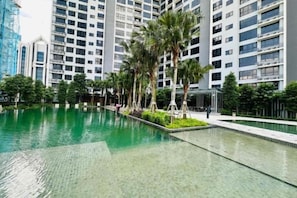 A swimming pool with a clear water surface, surrounded by a landscaped area with palm trees and a modern building complex in the background. - Agile SkyView Suites KL (Kuala Lumpur)