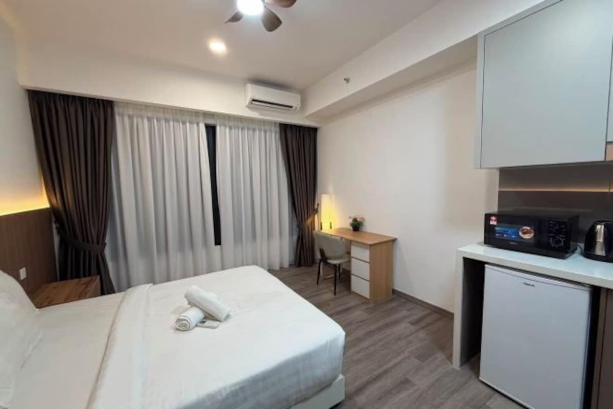 A hotel room with a bed, a desk, a chair, an air conditioning unit, and a small kitchenette.