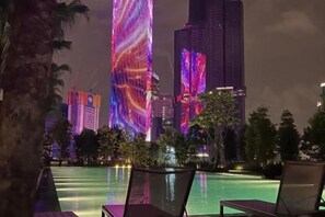 A nighttime view of a cityscape with illuminated skyscrapers and a pool area with lounge chairs. - Agile SkyView Suites KL (Kuala Lumpur)