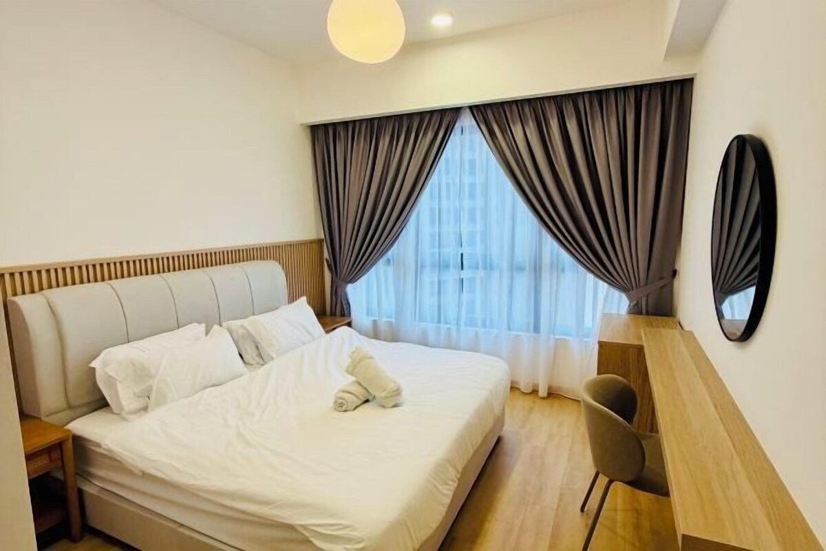 A modern hotel room with a large bed, a wooden bedside table, a chair, and a large window with curtains.