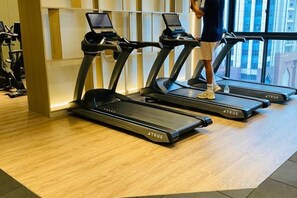 A gym with treadmills, a person walking on one, and a window in the background. - Agile SkyView Suites KL (Kuala Lumpur)