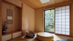 A traditional Japanese room with tatami flooring, a low wooden table, a woven round cushion, and a sliding shoji screen.