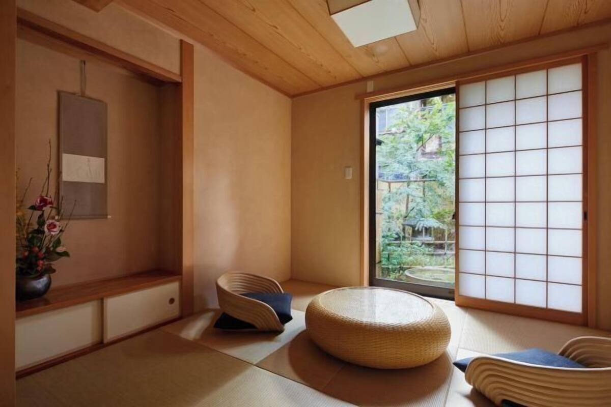 Una habitación japonesa tradicional con suelo de tatami, una mesa baja de madera, un cojín redondo tejido y un panel corredizo shoji.