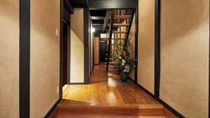 A hallway with wooden flooring, a staircase, and a potted plant.