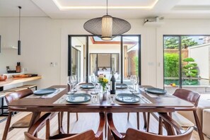 A modern dining area with a wooden table set for four, surrounded by chairs. - Oasis Residences Sanur – Family-Friendly 3-BR Villa with Private Pool & Garden (Bali)