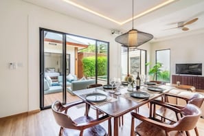 A dining area with a wooden table, chairs, and a hanging light fixture. - Oasis Residences Sanur – Family-Friendly 3-BR Villa with Private Pool & Garden (Bali)