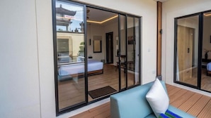 A modern room with a bed, a blue sofa, and a large sliding glass door leading to another room. - Oasis Residences Sanur – Family-Friendly 3-BR Villa with Private Pool & Garden (Bali)