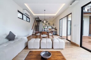 A modern living room with a sofa, ottomans, and a coffee table. - Oasis Residences Sanur – Family-Friendly 3-BR Villa with Private Pool & Garden (Bali)