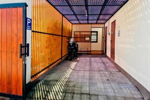 A narrow hallway with a motorcycle parked against a wall, a door with a 'P' sign, and a tiled floor. - Oasis Residences Sanur – Family-Friendly 3-BR Villa with Private Pool & Garden (Bali)