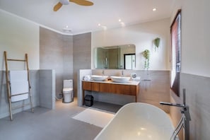 A modern bathroom with a freestanding bathtub, a large mirror, and a wooden vanity. - Oasis Residences Sanur – Family-Friendly 3-BR Villa with Private Pool & Garden (Bali)