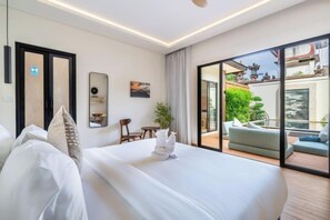 Una habitación de hotel moderna con una cama grande, una mesita pequeña y una silla. Cuenta con un balcón con vistas a zonas verdes y un edificio.