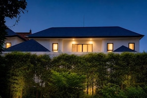 A two-story house with a dark roof, multiple windows, and a well-lit facade. - Oasis Residences Sanur – Family-Friendly 3-BR Villa with Private Pool & Garden (Bali)