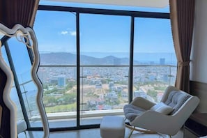 A room with a large window, a chair, and a view of a cityscape. - Meo's House - CSJ Seaside Apartment (Vung Tau)