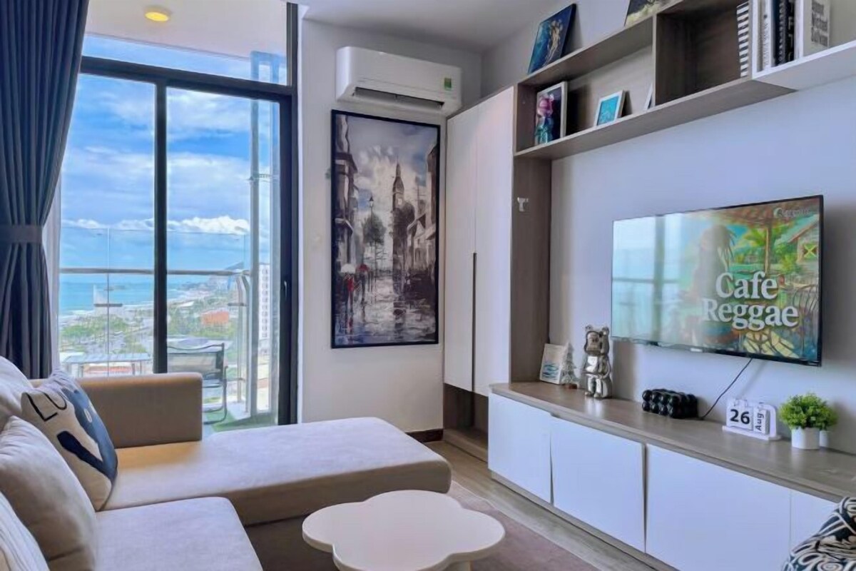 A modern living room with a sofa, a coffee table, a flat-screen TV, and a balcony view.