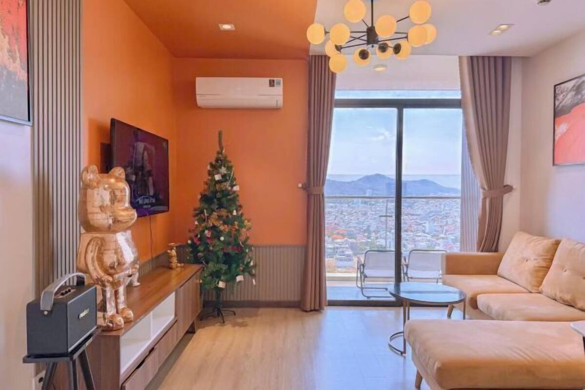 Un soggiorno con un divano, un tavolino, un albero di Natale e un'ampia finestra con vista sulla città.
