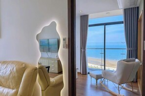 A modern hotel room with a large window, a sofa, a chair, and a flat-screen TV. - Meo's House - CSJ Seaside Apartment (Vung Tau)