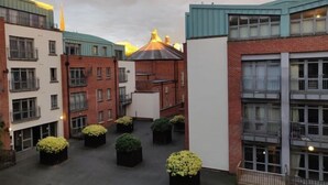 A courtyard with multiple buildings, including a red brick building and a white building with a blue roof. There are several black planters with green plants in the courtyard. - Beauchamp House - 2-Bed 2-Bath Apartment in Coventry City Centre by CovStays (Coventry)