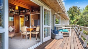 Una terraza de madera con asientos al aire libre, una estantería y un comedor con sillas y una mesa.