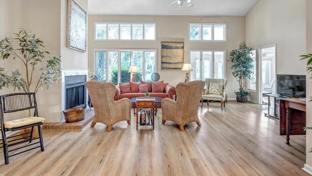 A spacious living room with a fireplace, large windows, and a ceiling fan. - Coastal Comforts - Peaceful condo w/ pool access (Ponte Vedra Beach)