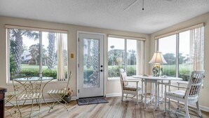 A spacious room with large windows, a dining area with white chairs, and a door leading outside. - Coastal Comforts - Peaceful condo w/ pool access (Ponte Vedra Beach)