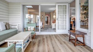 A spacious living area with a green sofa, a wooden coffee table, and a sliding glass door leading to a kitchen. - Coastal Comforts - Peaceful condo w/ pool access (Ponte Vedra Beach)