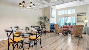 A dining area with a round table and chairs, a chandelier, and a fireplace in the background. - Coastal Comforts - Peaceful condo w/ pool access (Ponte Vedra Beach)
