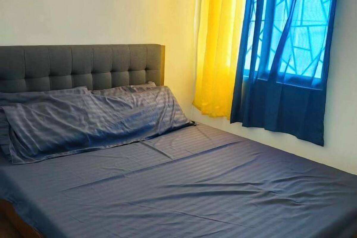 A bedroom with a bed, a headboard, and a window with yellow and blue curtains.
