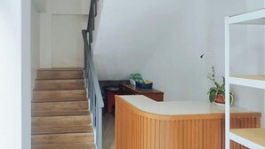 Una escalera de madera conduce a una zona de recepción con mostrador blanco y una planta en maceta.