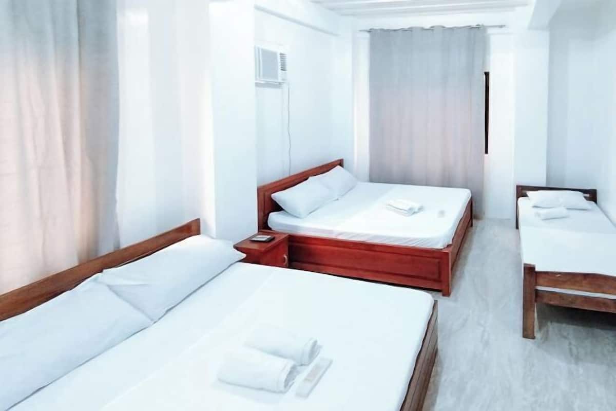 A hotel room with two single beds, a wooden headboard, a bedside table, and a window with curtains.