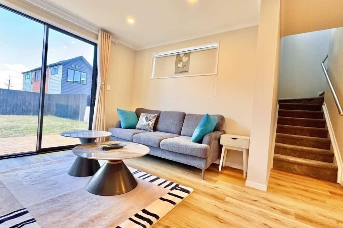 A modern living room with a grey sofa, a round coffee table, and a staircase.