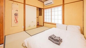 A traditional Japanese-style room with tatami flooring, a bed with white bedding, a shoji screen door, and a mounted air conditioner. - skytree Family Hotel (Tokyo)