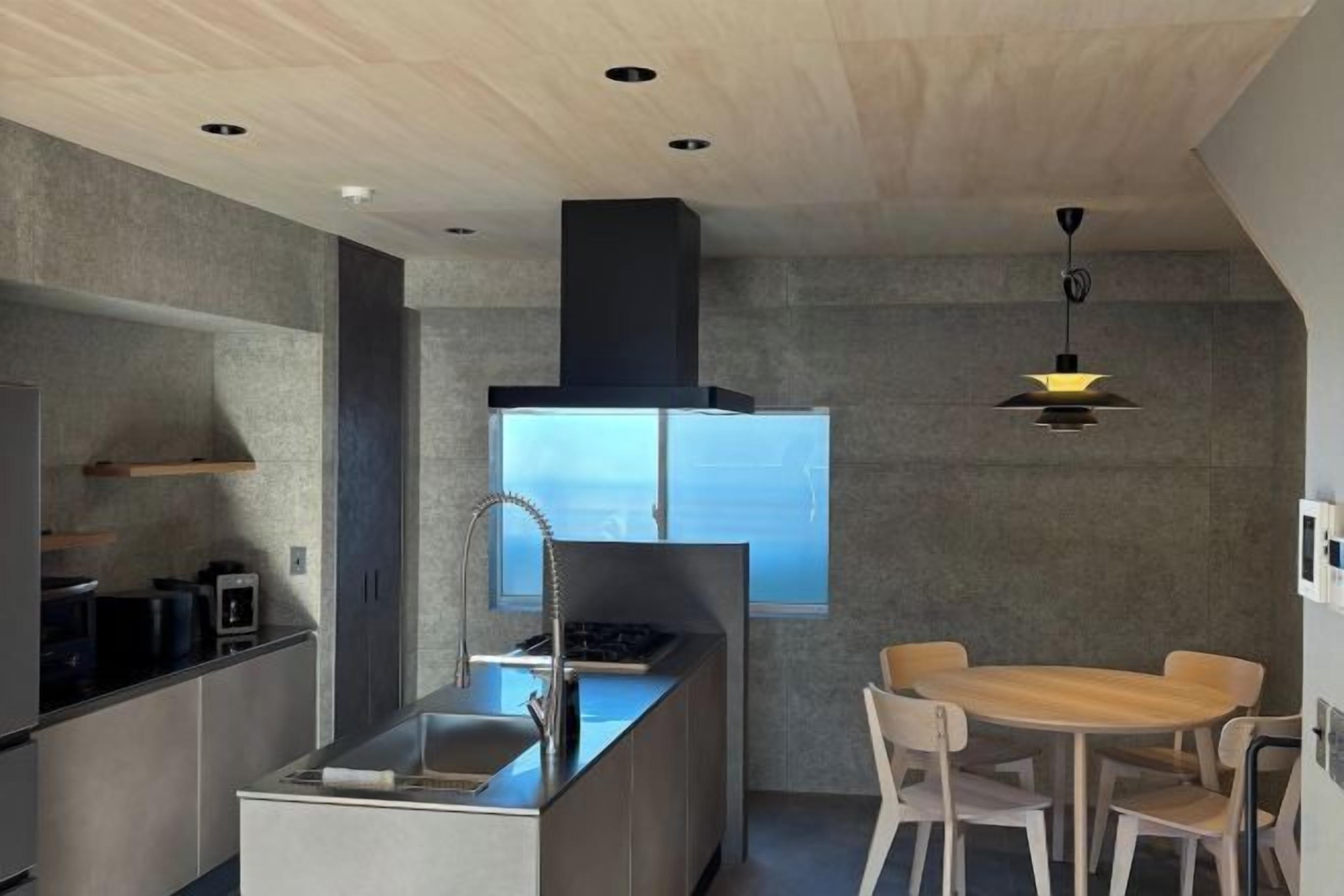 A modern kitchen with a central island, a dining area with a round table, and a large window providing natural light.