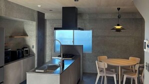 Una cocina moderna con una isla central, una zona de comedor con una mesa redonda y sillas, y un gran ventanal que ofrece luz natural.