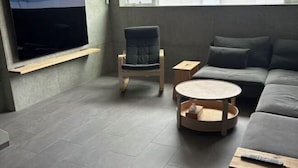 Una sala de estar moderna con un televisor de pantalla plana montado en la pared, un sofá gris, una mesa de centro redonda de madera y una silla negra.