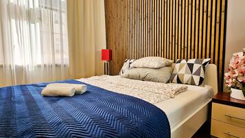 A modern hotel room with a large bed, a wooden slat wall, a red floor lamp, and a vase of flowers.