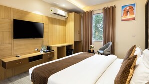 Een moderne hotelkamer met een groot bed, een flatscreen-tv, een bureau met stoel, en een raam met gordijnen.