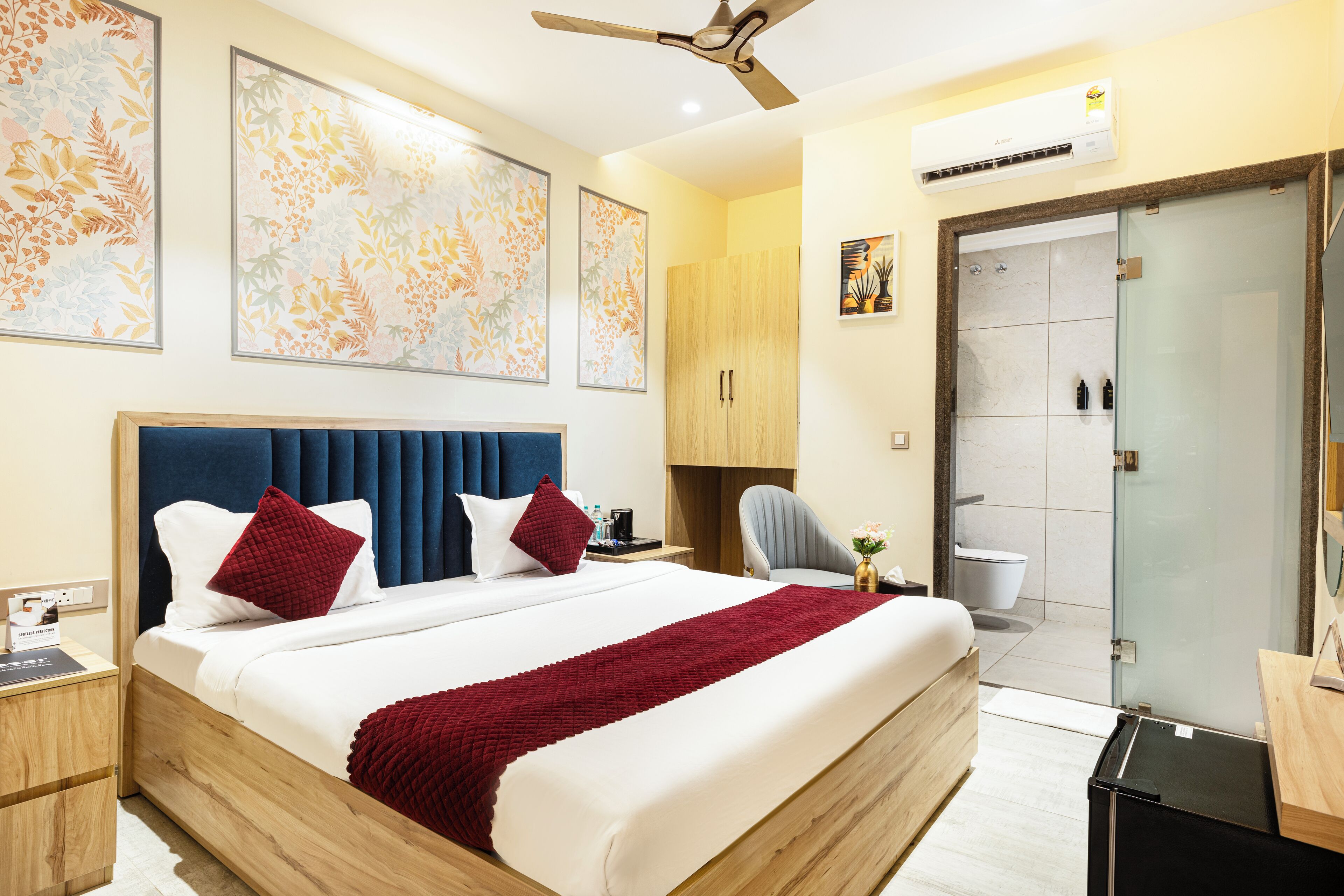 Una habitación de hotel con una cama grande, ventilador de techo, zona de ducha y obras de arte en las paredes.