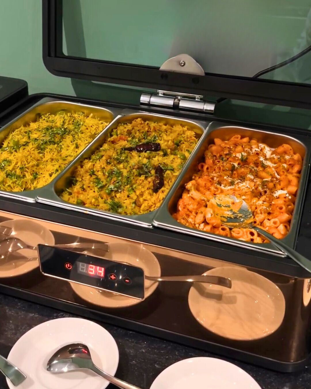 Un buffet con tre vassoi di cibo, una bilancia digitale e un cucchiaio.