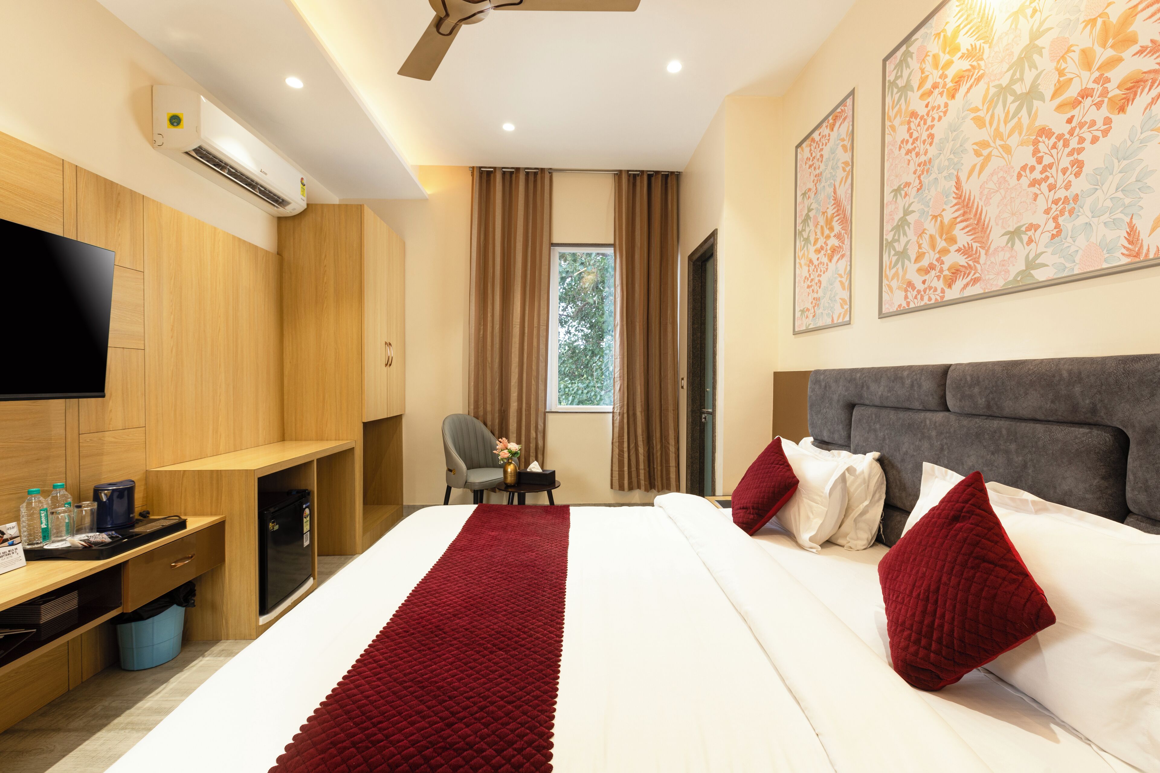 A hotel room with a bed, a desk, a chair, a television, and artwork on the walls.