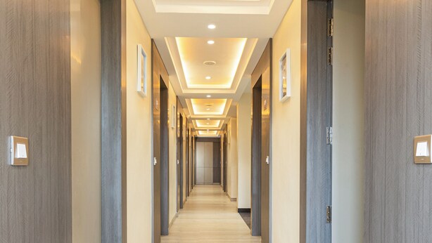 Een hotelgang met een lichtkleurig tapijt, houten wanden en genummerde deuren die de kamers aangeven.