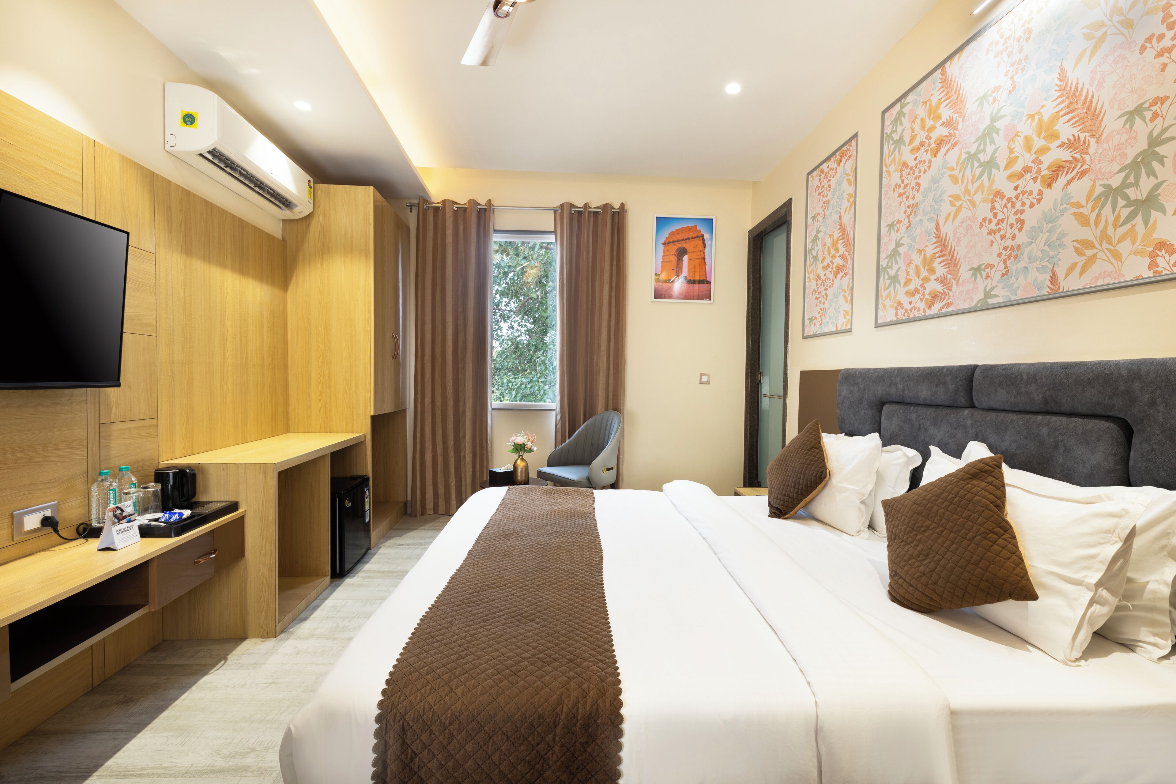 A hotel room with a large bed, a flat-screen TV, a desk with a computer, and a window with curtains.