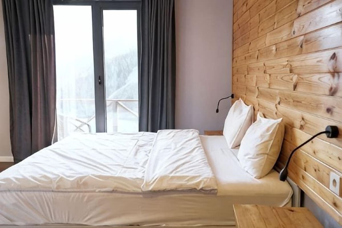 A bed with white bedding, a wooden headboard, and a view through a glass door.