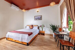 Een slaapkamer met een houten bed, nachtkastjes, een bureau met stoelen en een raam met gordijnen.