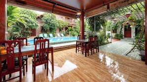 A wooden-floored patio with a pool, surrounded by lush greenery and traditional wooden furniture.