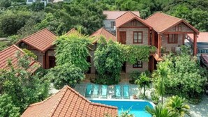 A villa with a swimming pool surrounded by lush greenery and mountains in the background.
