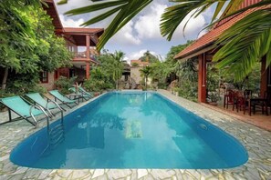 Une piscine entourée de chaises longues, de verdure et d’un bâtiment doté d’un toit rouge.